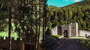 A stone castle with a central entrance, surrounded by a forested area and a paved pathway leading to it. - Castelpoggio Luxury Apartment (Ponte di legno)