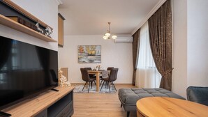 Una sala moderna con un televisor de pantalla plana, una mesa de comedor con sillas, un sofá gris y una mesa de centro de madera.