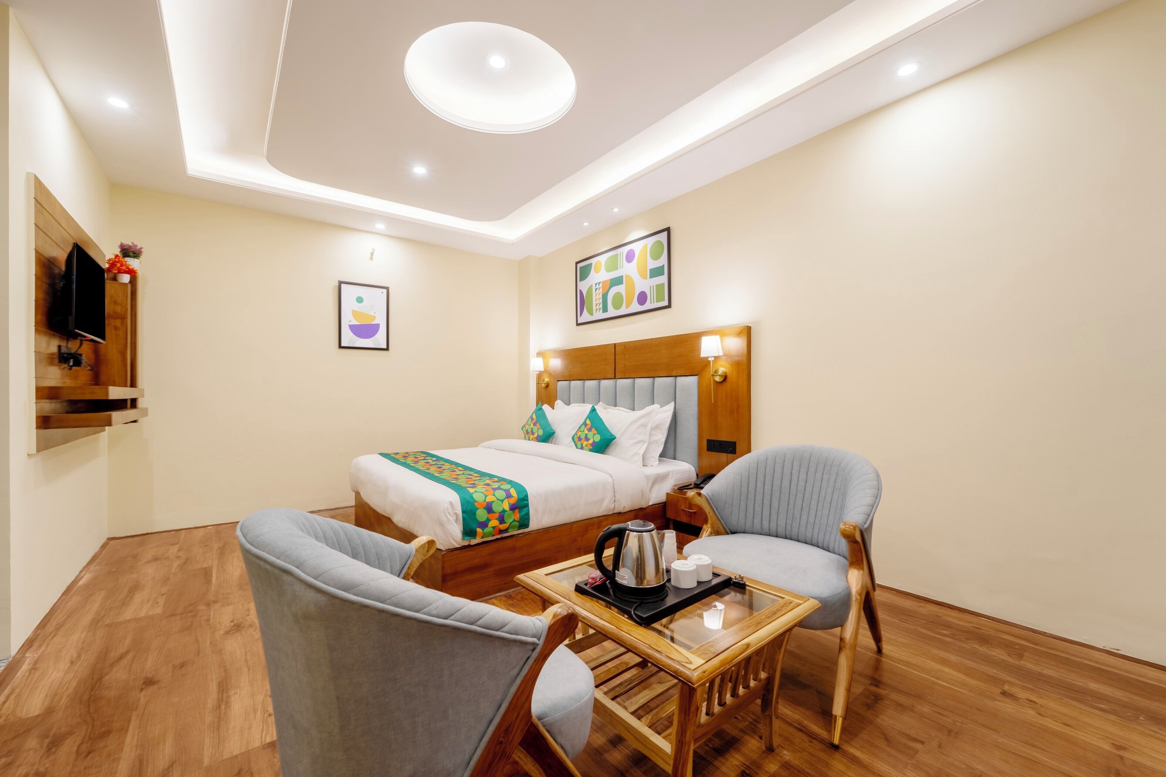 A hotel room with a bed, two armchairs, a small table with a tray, a television, and artwork on the walls.