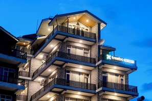 Un hotel de varios pisos con balcones, un letrero que dice "treebo THE TAKEY'S" y fachada de piedra.