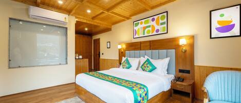A bedroom with a wooden ceiling, a large bed with a colorful blanket, a bedside table with a lamp, and a chair.