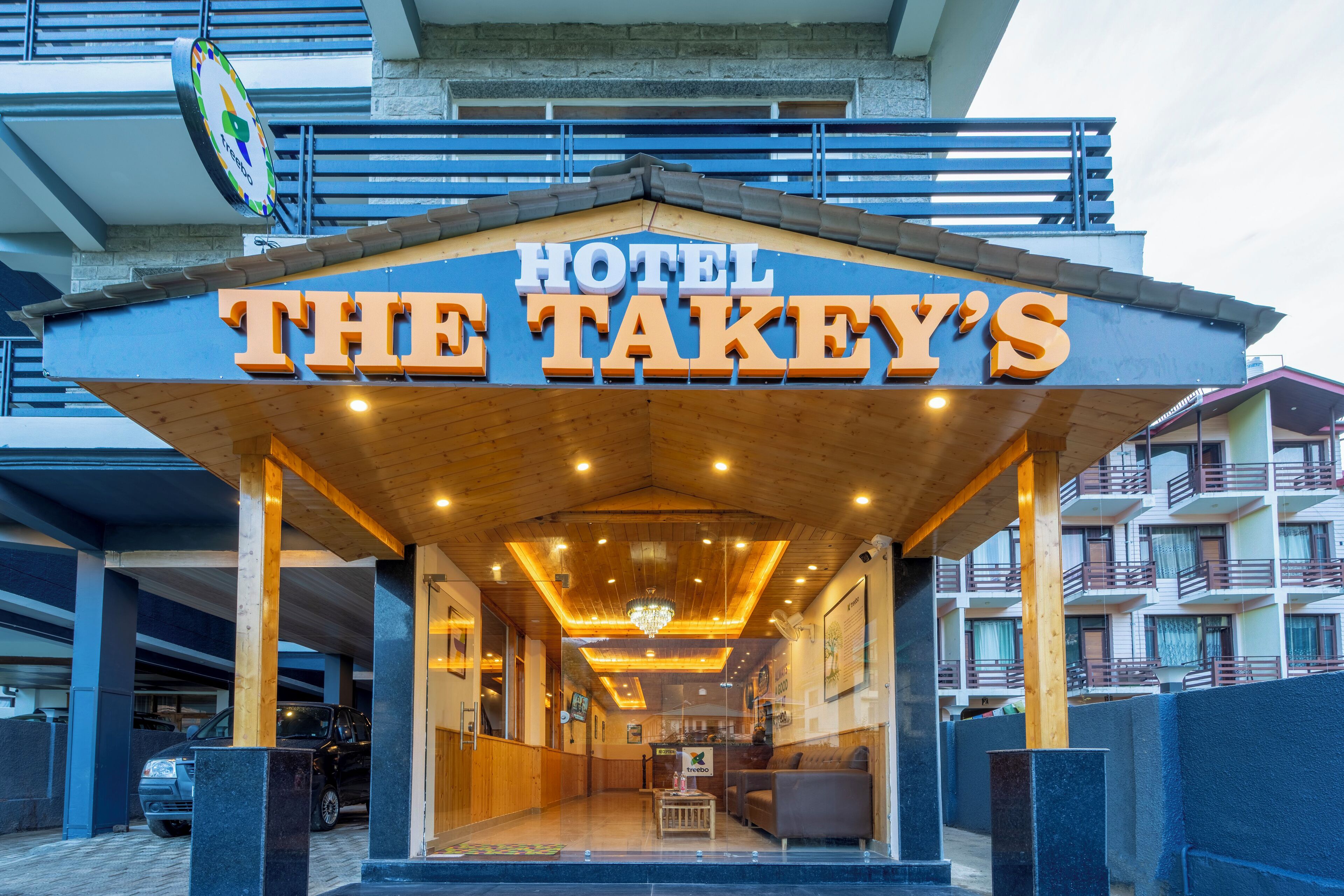 La entrada del Hotel The Takey's, con un área exterior cubierta, un mostrador de recepción y vistas del exterior del edificio.