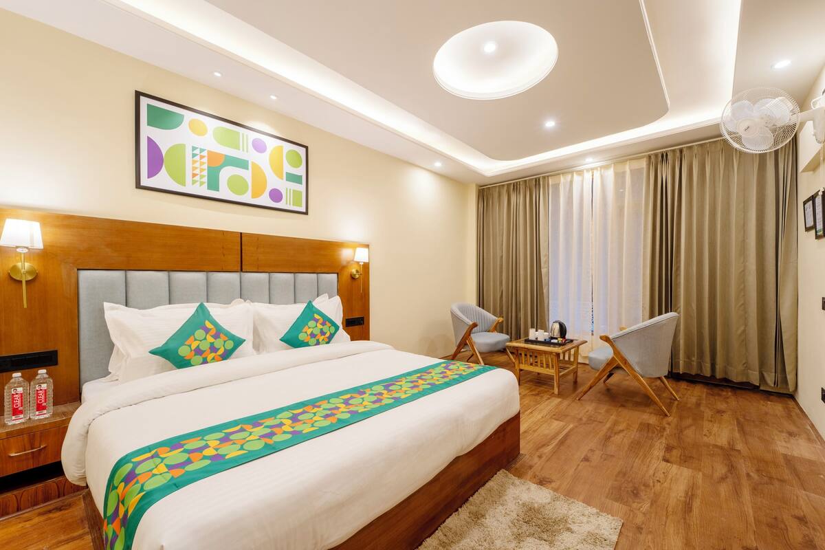 A hotel room with a large bed, two chairs, a small table, and a ceiling fan.