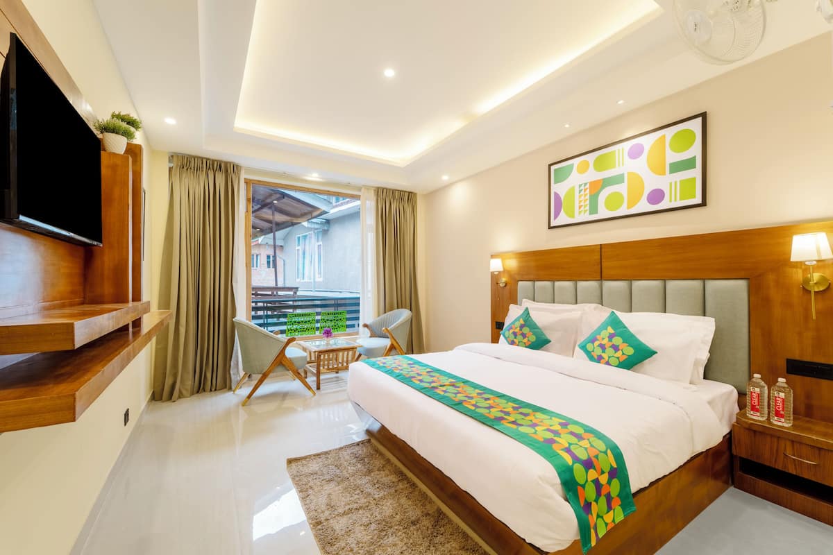 A modern hotel room with a large bed, a flat-screen TV, a dining area, and a balcony with a view.