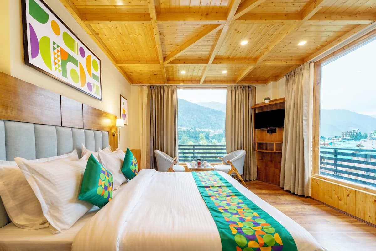 A hotel room with a large bed, a wooden ceiling, a view of mountains, and a TV on a wooden cabinet.