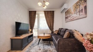 A modern living room with a flat-screen TV, a dark sofa, a round coffee table, and a painting on the wall.