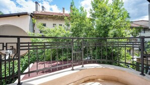 A balcony with a curved design, a metal railing, and a view of a building with a tiled roof and greenery.