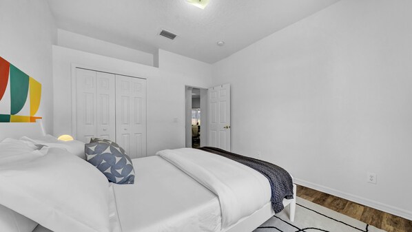 A bedroom with a bed, a nightstand, a lamp, and a door leading to another room.