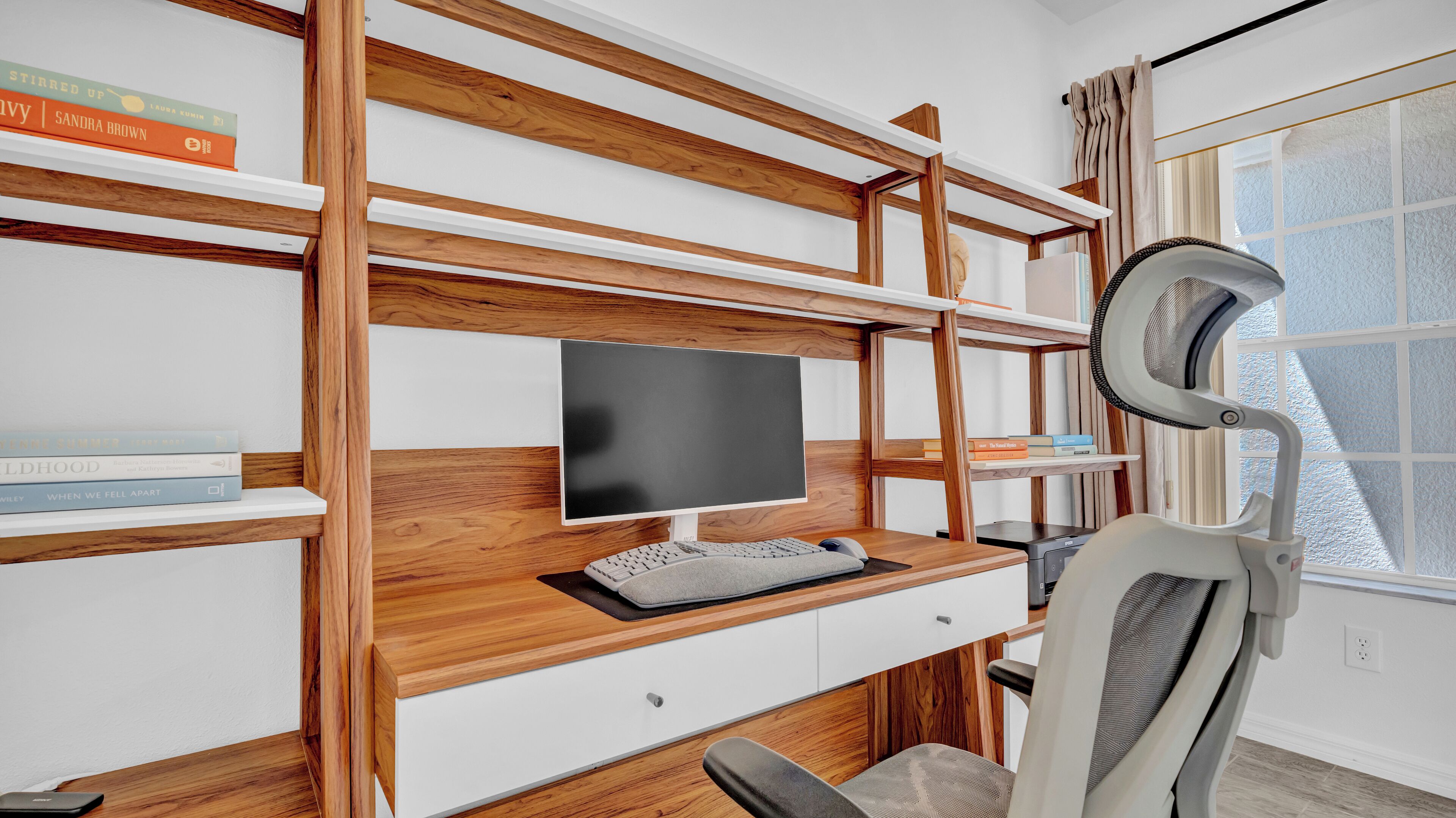 A modern home office with a wooden desk, a computer monitor, keyboard, and a chair.
