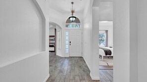 A hallway with a wooden floor, white walls, and a door leading to a bedroom.