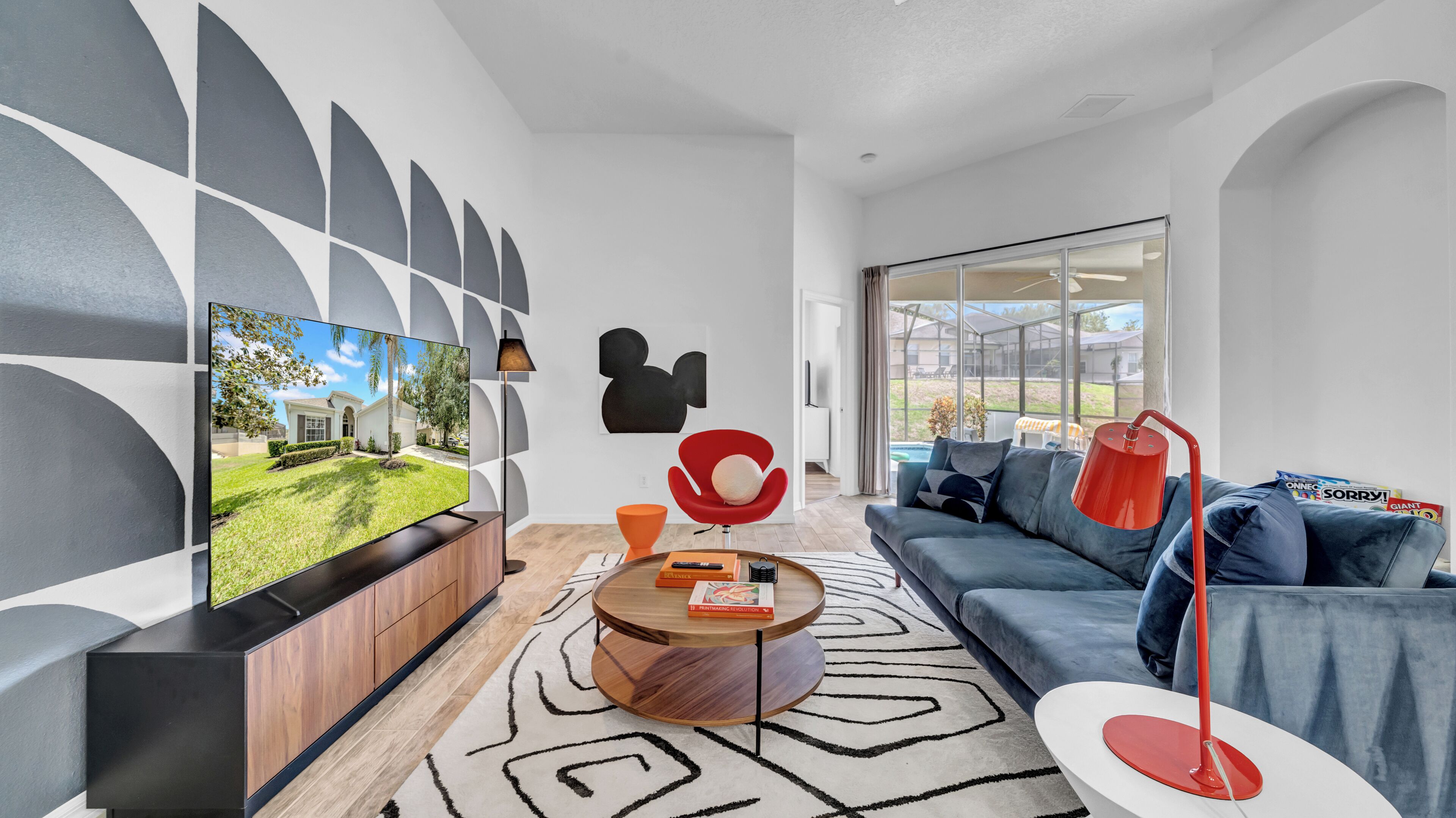 Een moderne woonkamer met een flatscreen televisie, een rode stoel, een blauwe bank en een groot raam.