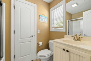 A bathroom with a white door, a toilet, a sink with a mirror, and a window with blinds.