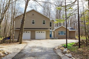 A two-story house with a garage, surrounded by trees and a gravel driveway.