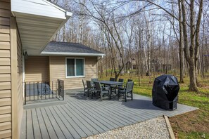 A deck with a table and chairs, a barbecue grill, and a house in the background.
