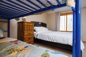Un letto a castello con una cassettiera in legno, una finestra con tende e un letto con coperta fantasia.