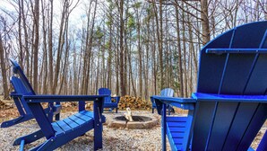 Uma área arborizada com área de estar externa, incluindo cadeiras Adirondack e uma lareira.