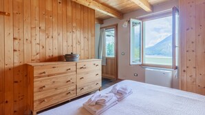 Een slaapkamer met houten lambrisering, een bed, een houten dressoir en een raam met uitzicht op de bergen.