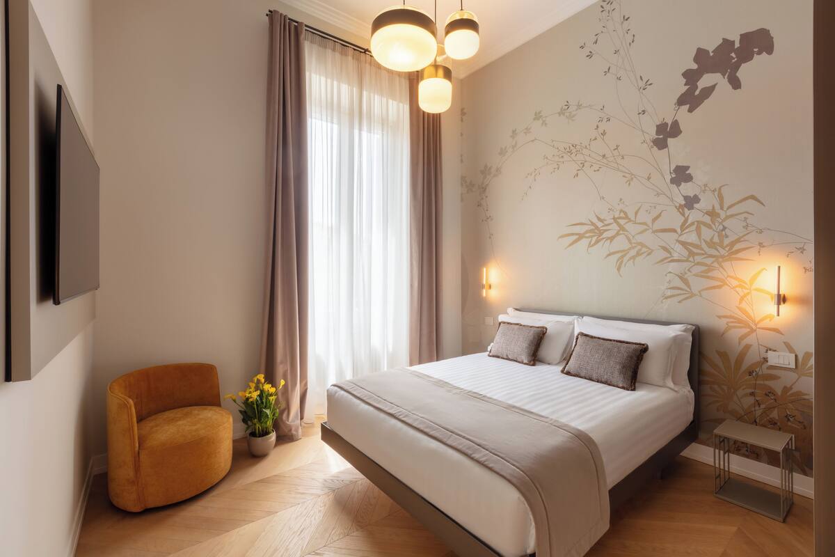 A modern bedroom with a large bed, a curved armchair, a small table, and a wall-mounted TV.