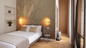 A hotel room with a bed, two wall-mounted lights, a small round table, and a suitcase. - Decòncept House (Rome)