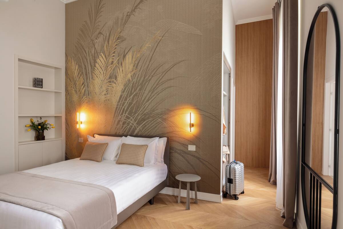 A hotel room with a bed, two wall-mounted lights, a small round table, and a suitcase.