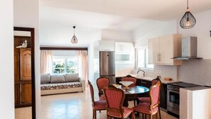 A modern kitchen with a dining area, featuring a round table, chairs, and a built-in oven. - Alnes Hotel (Sarande)