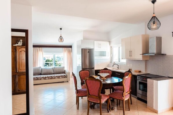 A modern kitchen with a dining area, featuring a round table, chairs, and a built-in oven. - Alnes Hotel (Sarande)