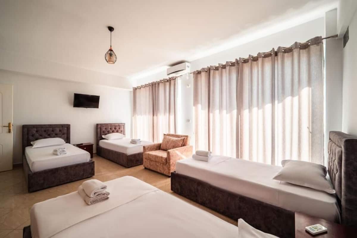 A hotel room with two beds, a sofa, a chair, a TV, and an air conditioning unit.