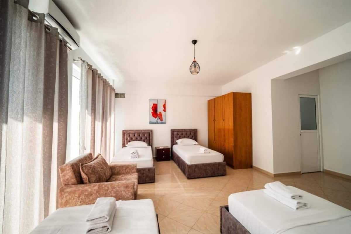 A hotel room with two beds, a sofa, a wooden wardrobe, and a painting on the wall.