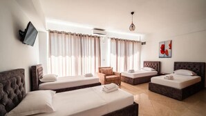 A hotel room with two beds, a sofa, a chair, and a TV mounted on the wall. - Alnes Hotel (Sarande)