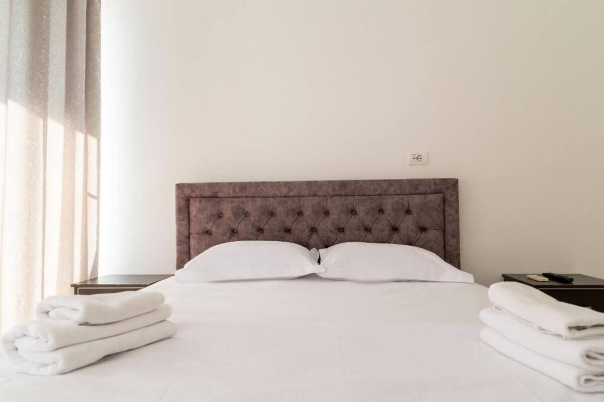 A neatly made bed with a tufted headboard, white pillows, and folded towels on either side.