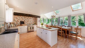 A spacious kitchen with a central island, wooden flooring, and large windows offering views of greenery.