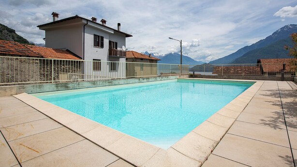 Ein rechteckiger Pool mit einer gefliesten Terrasse, umgeben von einem weißen Zaun, vor einer Berglandschaft und blauem Himmel.
