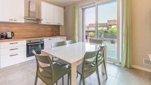 A modern kitchen with white cabinets, a stainless steel range hood, and a dining area with a white table and green chairs.