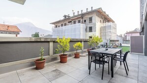 A rooftop terrace with a table and chairs, potted plants, and a view of a building under construction.