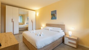 A bedroom with a bed, bedside tables, a wooden nightstand, a mirror, and a painting on the wall.