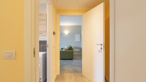 A hallway leading to a room with a washing machine, a green sofa, and a light switch on the wall.