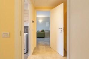 Un corridoio che porta a una stanza con lavatrice, un divano verde e un interruttore a muro.