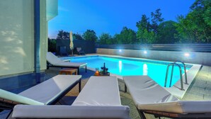 A poolside area with lounge chairs, a pool, and a view of trees.