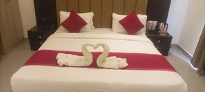 A hotel room with a large bed, two nightstands, a red throw blanket, and a heart-shaped towel decoration. - Hotel Grand Empire (Agra)
