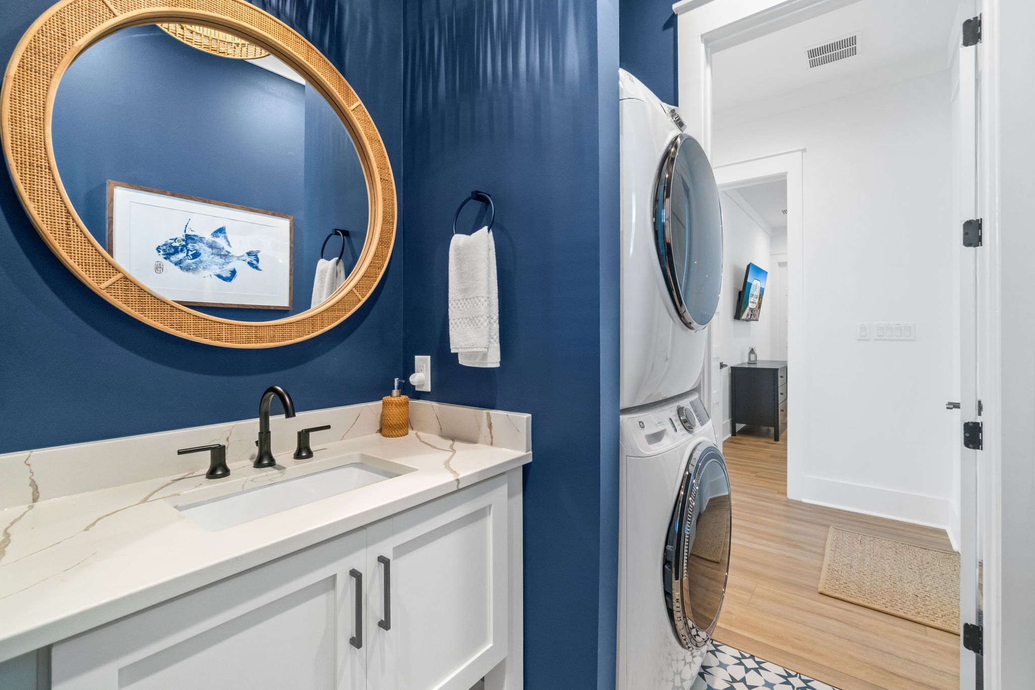 A bathroom with a blue wall, a white sink with a marble countertop, a round mirror, and a washing machine.
