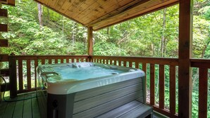 Een hottub op een houten terras met uitzicht op een bos.