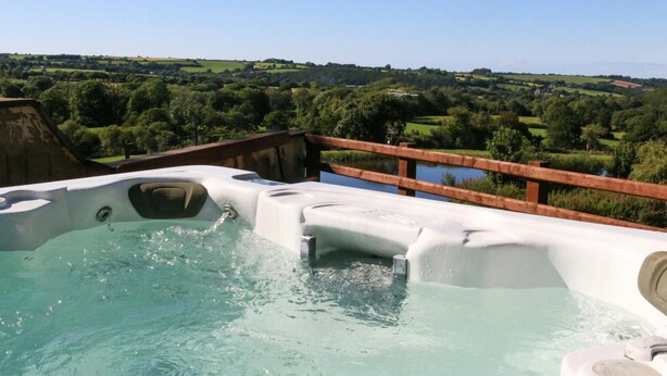A hot tub with a wooden deck and a scenic view of a green landscape. - Yr Onnen, Aberaeron - Two Bedroom Cottage, Sleeps 4 (Llanarth)