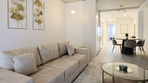 Un salon moderne avec un canapé beige, une table basse en verre et deux œuvres d’art encadrées accrochées au mur.