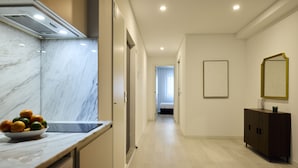 Un couloir d’hôtel moderne avec un comptoir en marbre, un panier de fruits, un meuble en bois foncé et un tableau encadré au mur.