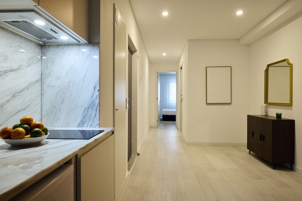 A modern hotel corridor with a marble countertop, a bowl of fruit, a dark wooden cabinet, and a framed picture on the wall.