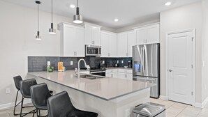 A modern kitchen with white cabinets, a large island with bar stools, stainless steel appliances, and pendant lighting.