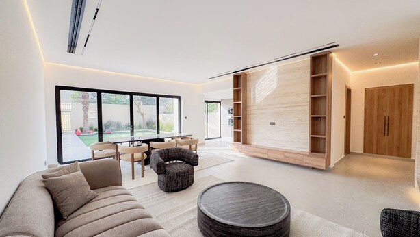 Ein modernes Wohnzimmer mit einer großen Couch, einem runden Couchtisch und einem Essbereich mit Stühlen und einem Tisch. Ein großes Fenster bietet einen Ausblick ins Freie.