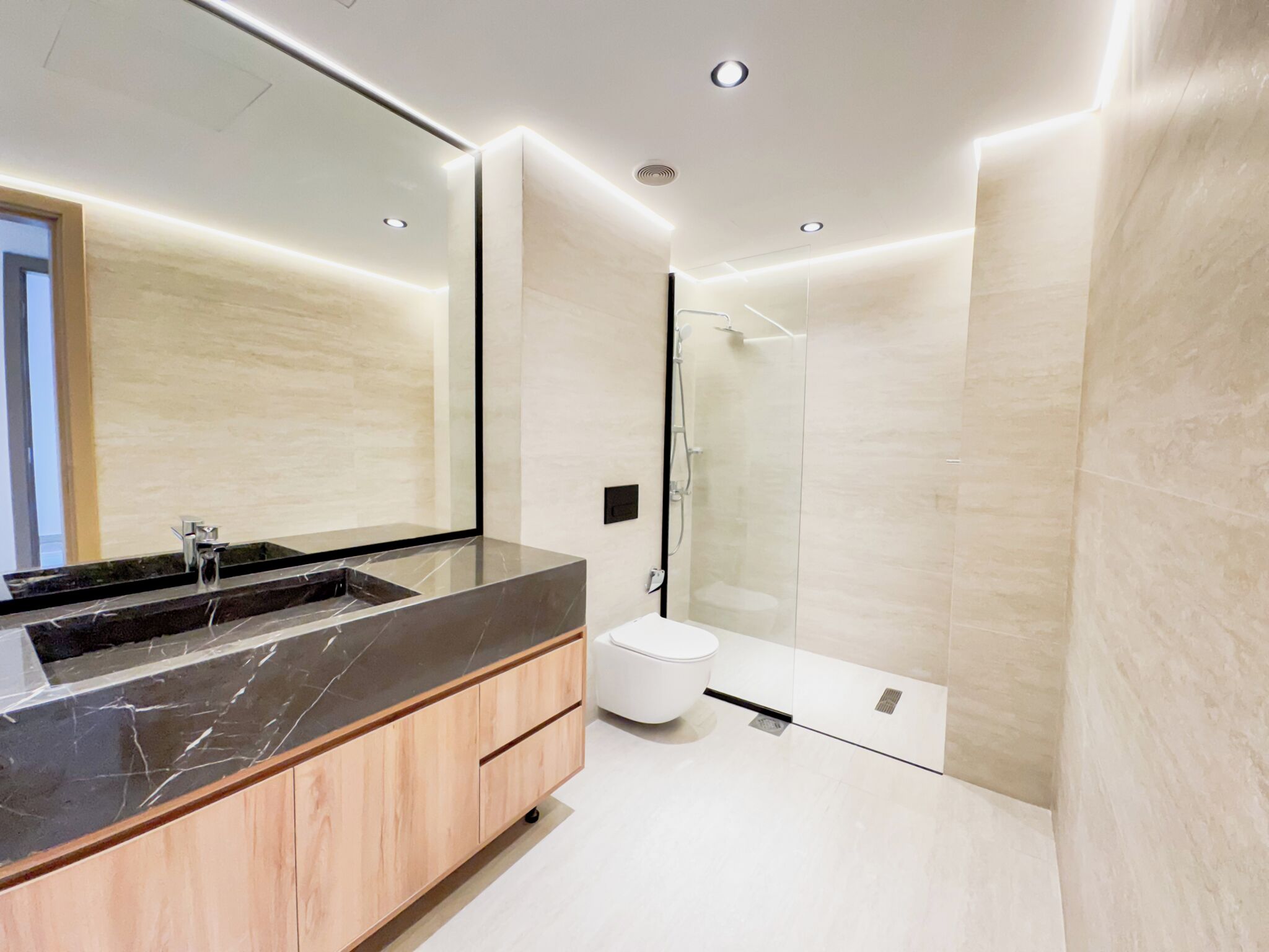A modern bathroom with a large mirror, a black marble sink, a white toilet, and a glass shower enclosure.