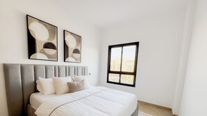 Ein modernes Schlafzimmer mit einem großen Bett, einem grauen, gepolsterten Kopfteil und zwei abstrakten Wandbildern.