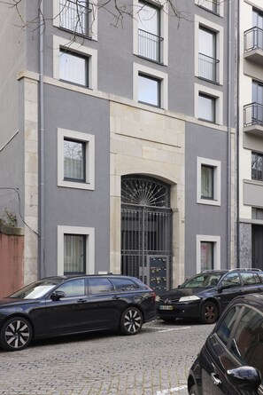 A multi-story building with a modern facade, a gated entrance, and parked cars on the street.